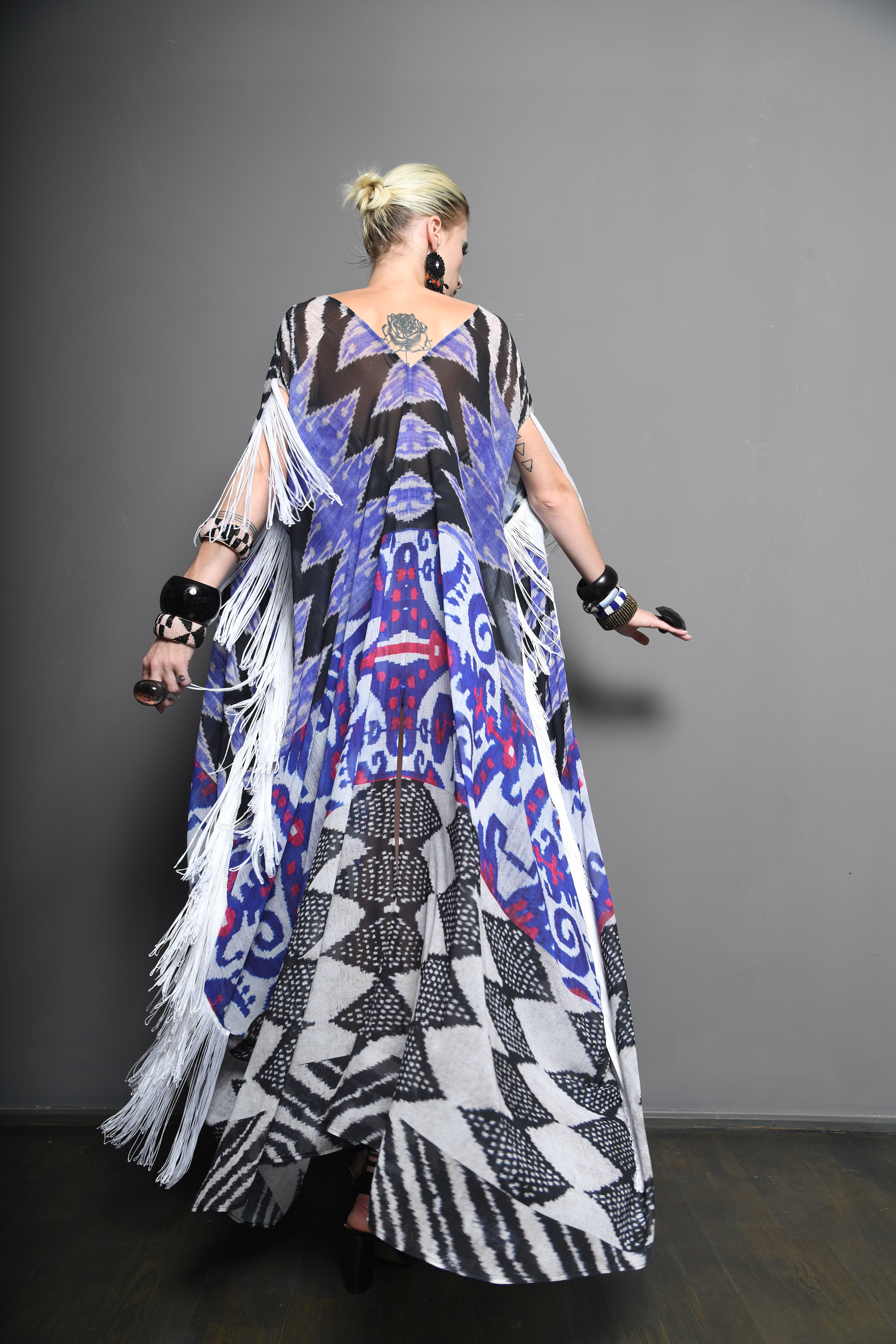 Person wearing a colorful patterned dress with fringe on a gray background